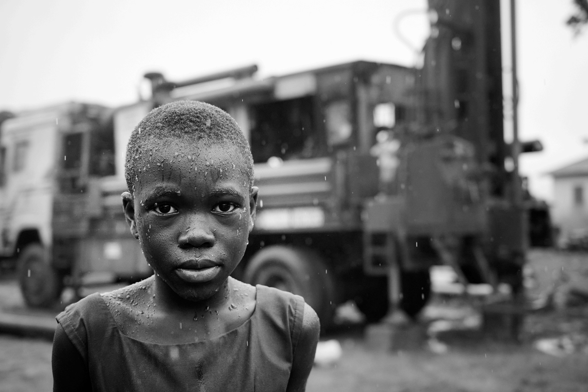 The rain doesn’t deter onlookers standing in front of the drilling rig, drilling for clean water. Anfoega Bume.